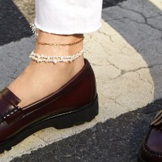 Close-up of a woman's ankle adorned with a pearl anklet, paired with a gold chain and white distressed jeans, showcasing fashionable jewelry suitable for summer and casual outings.