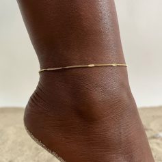 Close-up of a delicate gold anklet on dark-skinned ankle, perfect for beachwear, summer outfits, and stylish accessories. High-quality jewelry emphasizing elegance and style.