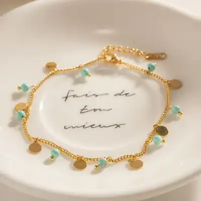 Gold bracelet featuring small turquoise beads and round gold charms, perfect for stylish accessorizing and international fashion.