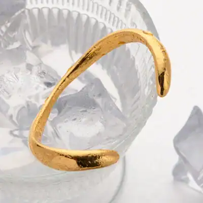 Elegant gold cuff bracelet displayed on ice cubes, perfect for luxury jewelry shopping. Ideal for stylish accessories and gift ideas.