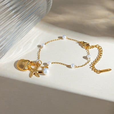 Delicate gold chain necklace with seashell and starfish pendants, accented with white pearls, ideal for beach-inspired fashion and accessorizing stylish looks.