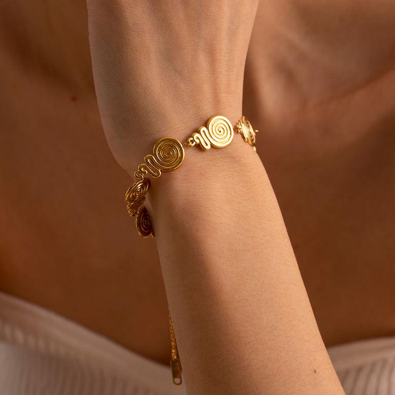 A close-up of a stylish gold spiral bracelet on a woman's wrist, showcasing intricate swirl designs and luxurious craftsmanship, perfect for enhancing your jewelry collection.
