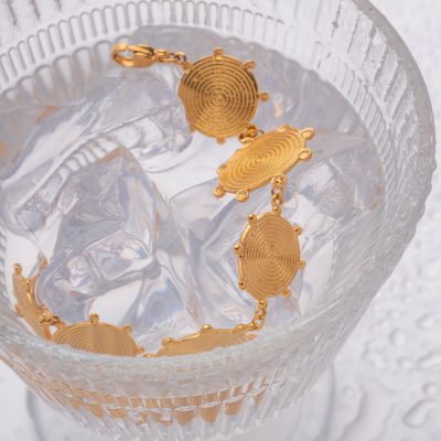 Gold bracelet featuring circular engraved motifs, delicate chain links, stylish accessory for women, perfect for fashion or special occasions.