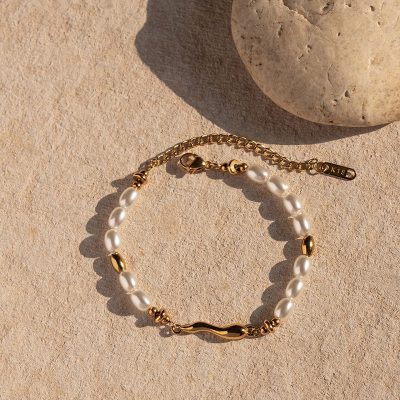 Gold and freshwater pearl bracelet on sandy surface with shadow, perfect for stylish jewelry and accessory shopping.