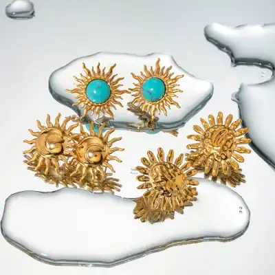 Elegant gold sunburst earrings with turquoise centers showcased on decorative glazed pottery. Perfect for adding a touch of luxury and style to any jewelry collection.
