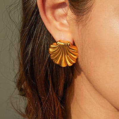 Close-up of a gold shell-shaped earring worn on a woman's ear, showcasing luxurious jewelry accessories for an enhanced fashion statement.