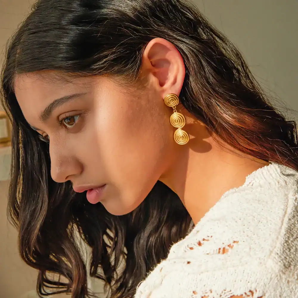 Close-up of woman wearing gold spiral earrings, showcasing trendy and luxurious jewelry from Monalisa Store for sophisticated style and accessorizing.