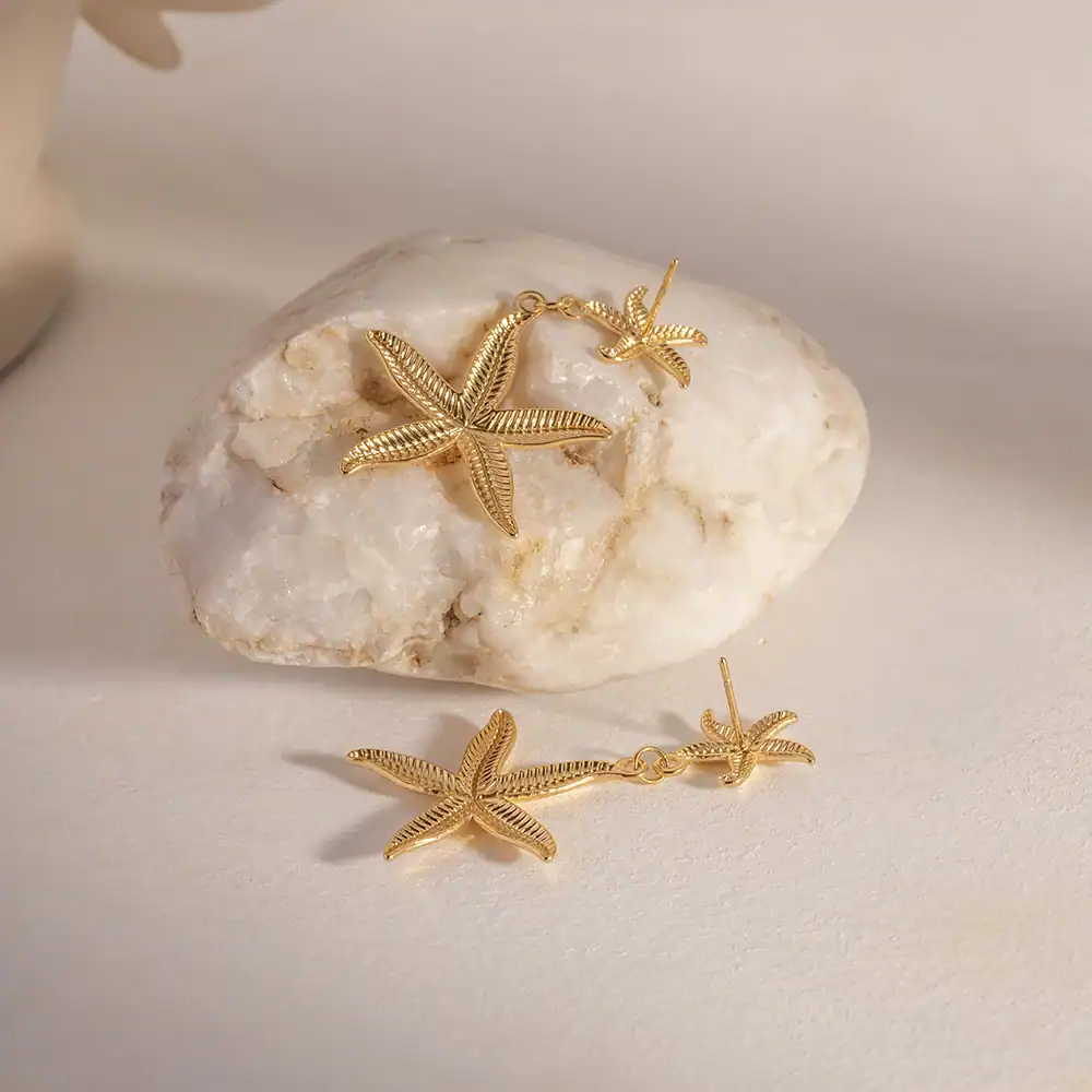 Elegant gold starfish earrings and necklace set on natural white stone, perfect for beach or summer themed jewelry collections. High-quality craftsmanship and stylish design for women.
