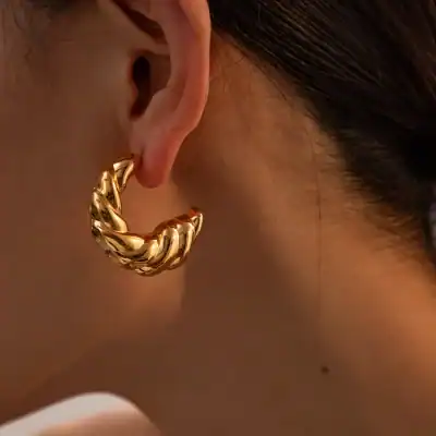 Close-up of a stylish gold hoop earring worn on a woman's ear, showcasing high-quality jewelry and trendy design. Perfect for fashion-forward accessories and gifting occasions.