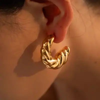 Close-up of a gold hoop earring with a thick chain design, worn on a person's ear. Perfect for fashion-forward and trendy accessories.