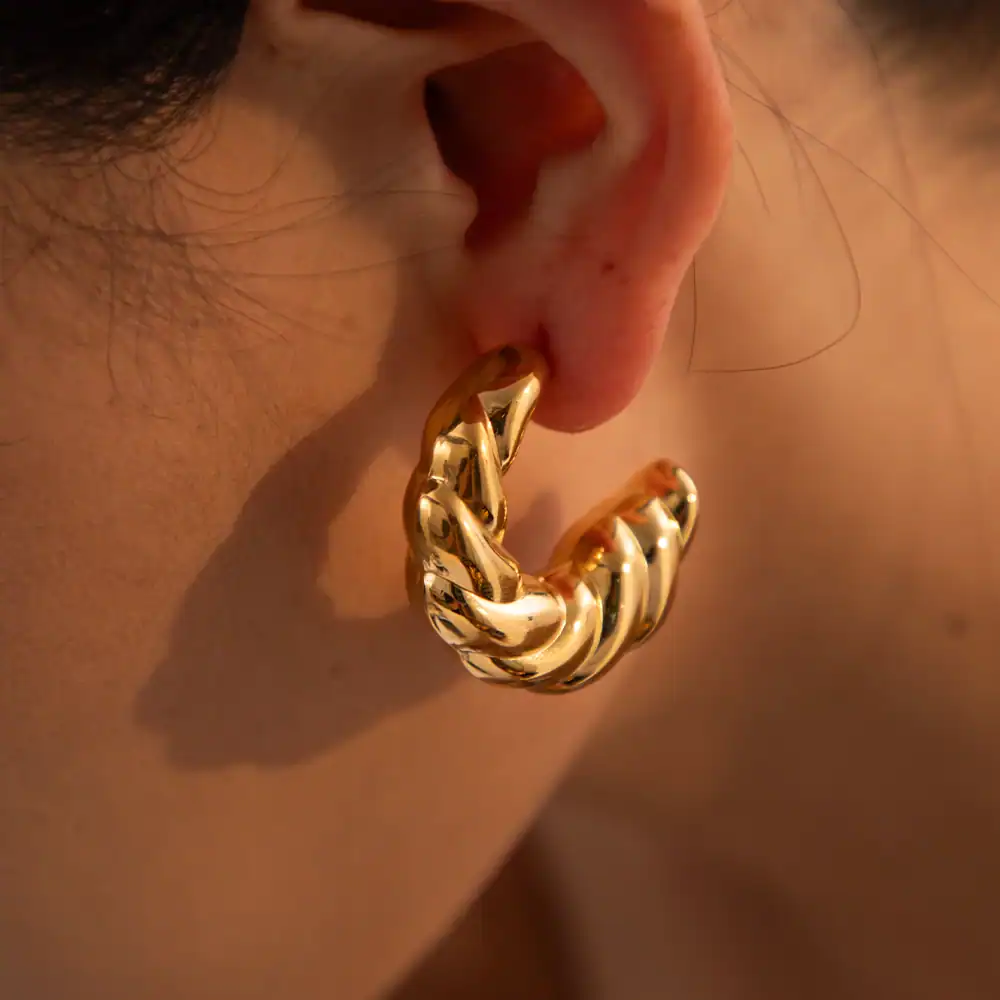 Close-up of a gold hoop earring with a thick chain design, worn on a person's ear. Perfect for fashion-forward and trendy accessories.