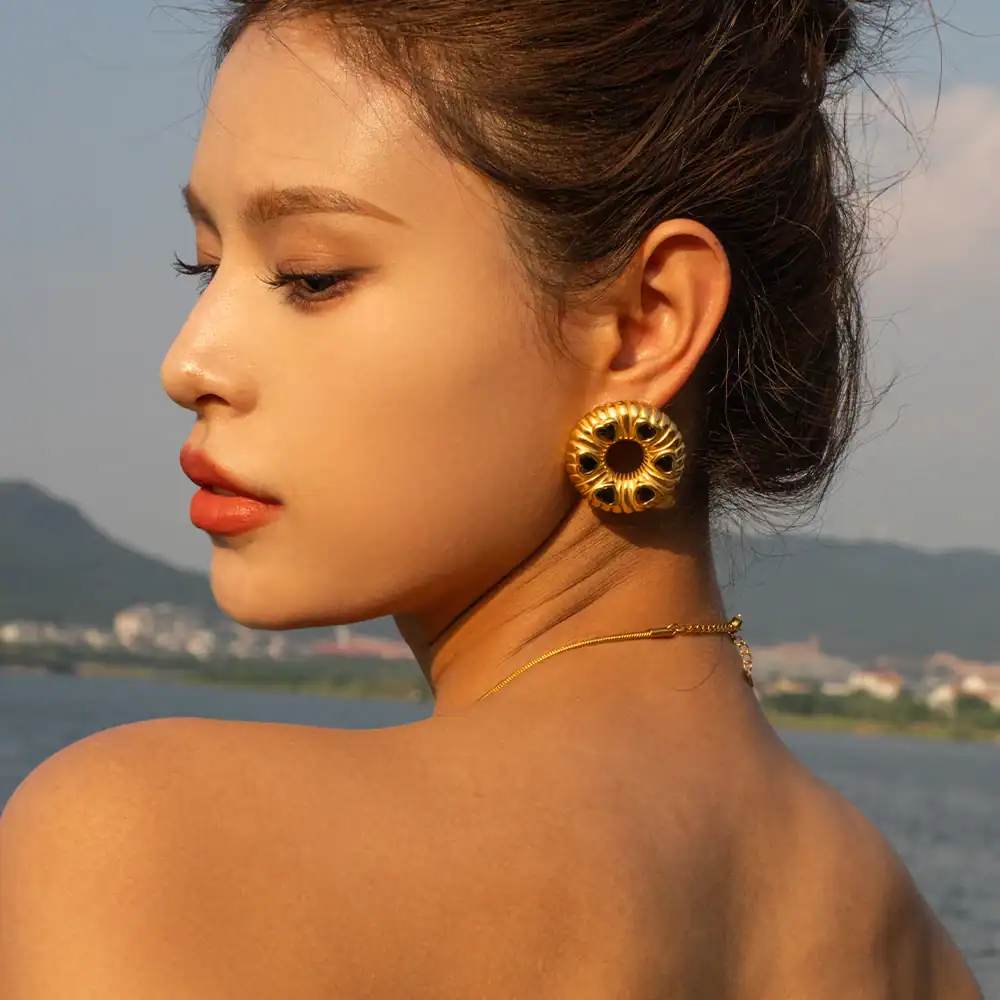 Delicate gold earrings and necklace showcased on a woman with a scenic water and mountain background, perfect for fashion jewelry lovers.