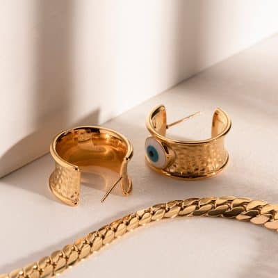 Gold jewelry featuring an eye design cuff bracelet, matching earrings, and a gold chain for chic accessorizing.