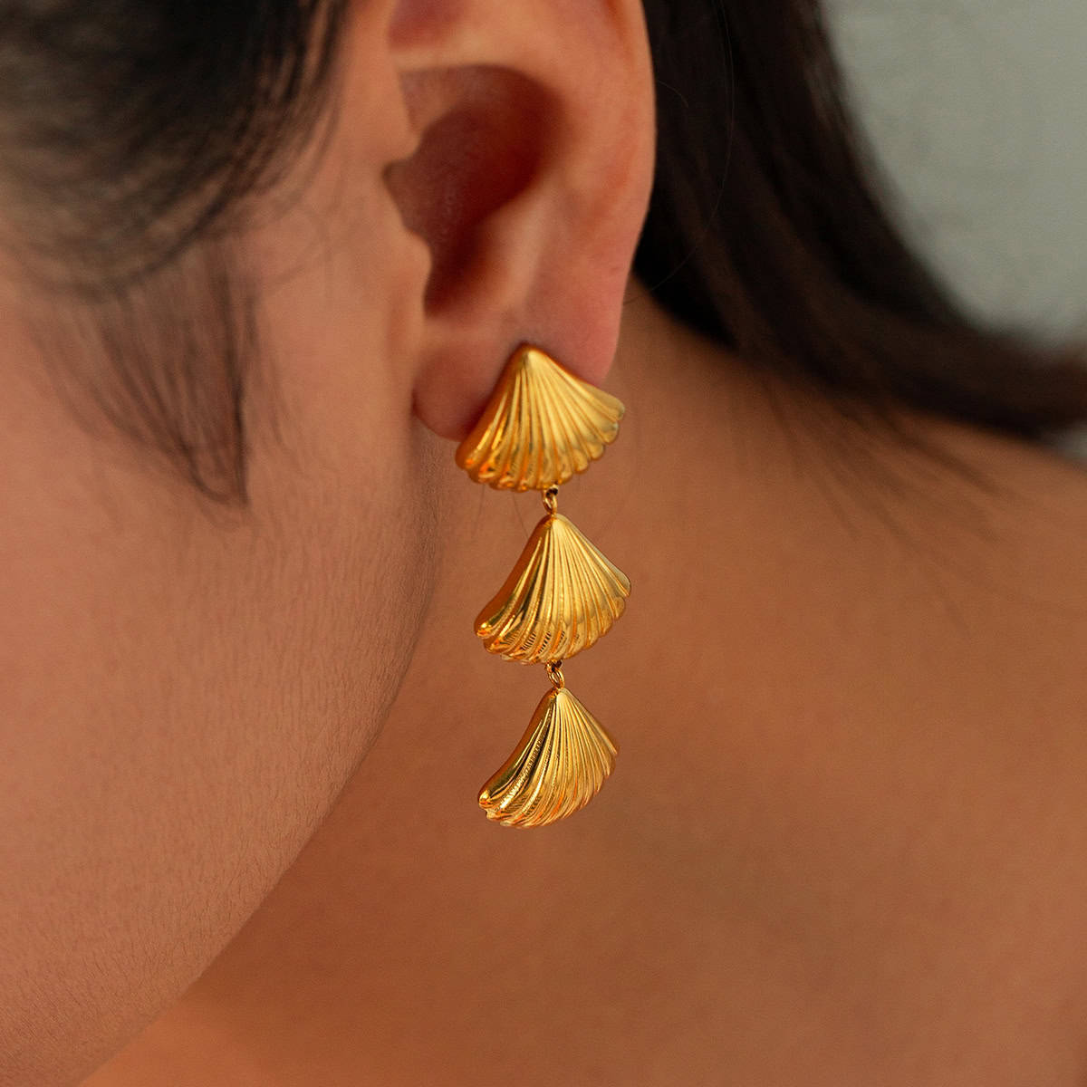 Close-up of gold shell-shaped dangle earrings worn on a woman's ear, showcasing stylish jewelry perfect for fashion accessories and enhancing your look.