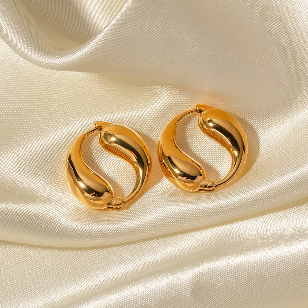 Luxurious gold hoop earrings displayed on silky beige fabric, perfect for elegant accessories and fashion statements.