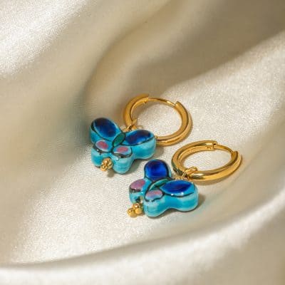 Colorful butterfly-shaped earrings with blue, pink, and black details, featuring gold hoops. Perfect for stylish accessories, offering a vibrant look for any occasion.