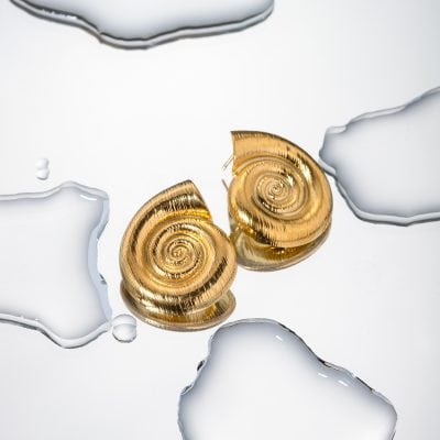 Stunning gold shell earrings showcased on a reflective surface, accented by artistic white and silver abstract elements. Ideal for fashion-forward jewelry lovers.