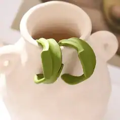 Stylish green eye-shaped earrings on a white ceramic vase.