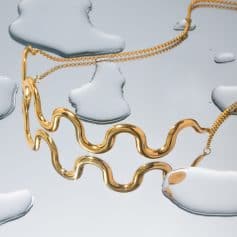 Gold jewelry with unique wavy design on a reflective surface with water puddles, highlighting luxury accessories perfect for skincare, beauty, and wellness enthusiasts.