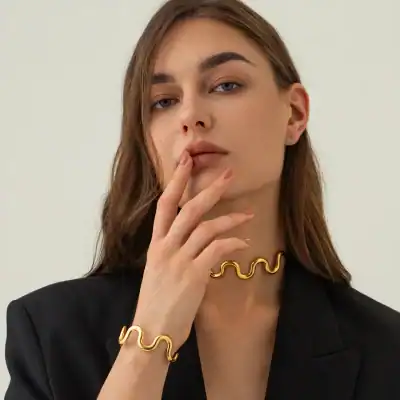 Vibrant gold jewelry including a necklace and bracelet with a wavy design, worn by a woman with flawless skin, brown hair, and minimalist makeup for a luxurious look.