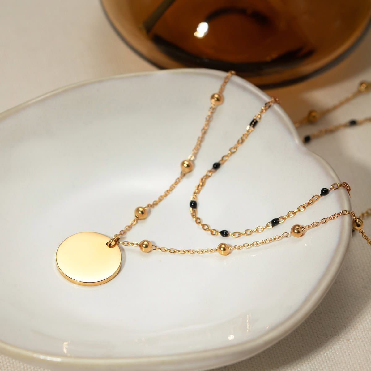 Stylish gold necklace featuring black beads displayed on a white ceramic dish, perfect for accessorizing any outfit. Shop high-quality jewelry at Monalisa Store for a sophisticated look.