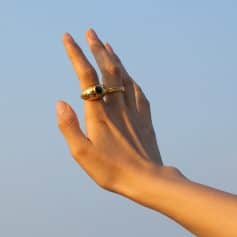 Close-up of a hand wearing elegant gold rings, featuring black gemstone accents, showcasing fashionable jewelry at Monalisa Store for stylish accessories.