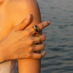 Close-up of a woman's hand wearing stylish gold rings with a black gemstone, set against a scenic water background, perfect for showcasing luxury jewelry and fashion accessories.