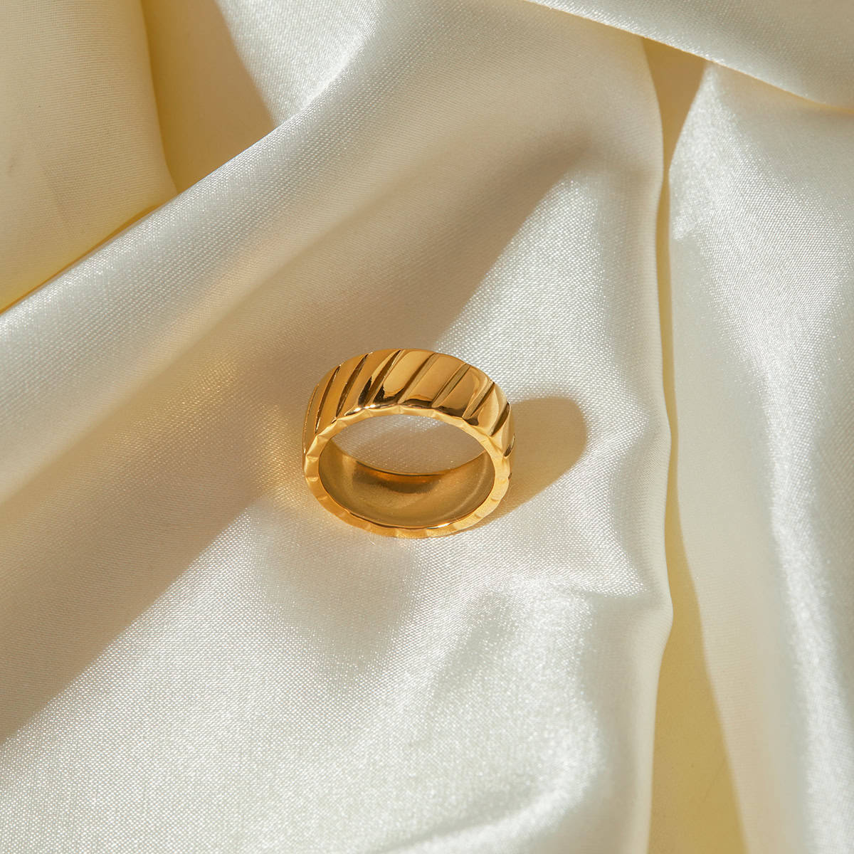 Luxurious gold ring with a textured, modern design displayed on silky satin fabric, ideal for fashion and jewelry enthusiasts.