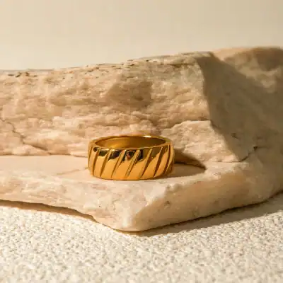Close-up of a shiny gold ring with diagonal grooves, displayed on a textured stone surface for a luxurious jewelry presentation.