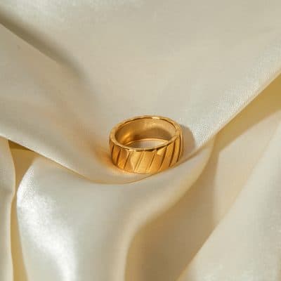 Close-up of a stylish gold ring with diagonal groove design, resting on smooth ivory satin fabric, ideal for jewelry lovers and those seeking luxury accessories from Monalisa Store.