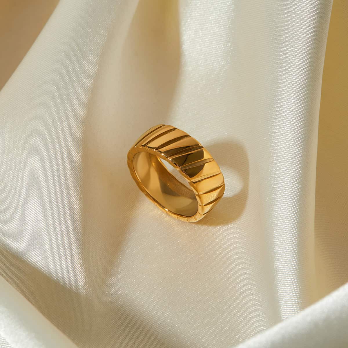 High-quality gold ring featuring a contemporary ribbed pattern, displayed on luxurious ivory silk fabric for an upscale jewelry presentation, perfect for modern jewelry collections.