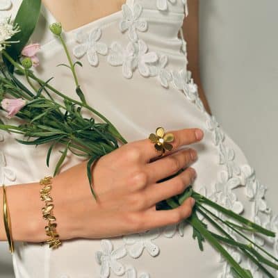 Beautiful gold flower ring and bracelet showcased with fresh flowers against a white embroidered dress, emphasizing luxury jewelry and bridal accessories at Monalisa Store.