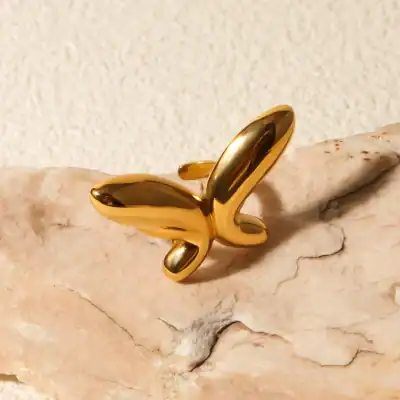 A shiny gold butterfly-shaped ring displayed on a natural stone, showcasing fashionable jewelry designed for those who love unique and trendy accessories.