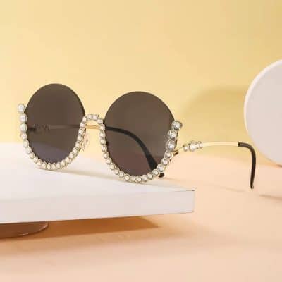 Luxury sunglasses adorned with pearls and rhinestones, featuring dark lenses and stylish gold accents, perfect for a fashionable look.