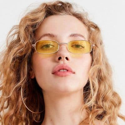Elegant woman wearing yellow-tinted sunglasses with wavy blonde hair, showcasing trendy eyewear. Perfect for fashion-forward individuals seeking stylish optical accessories.