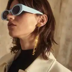 Alt text: Stylish woman wearing oversized white sunglasses with gold chain earrings featuring 