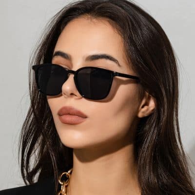 Close-up of fashionable black sunglasses worn by a woman with long dark hair, highlighting trendy eyewear designs available at Monalisa Store.