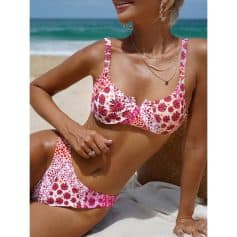 Woman in floral bikini top and bottom on the beach, showcasing stylish swimwear and layered jewelry, perfect for summer beach fashion.
