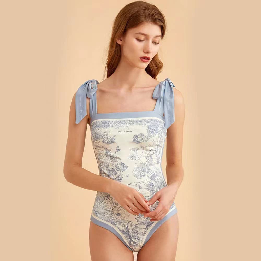 A sophisticated floral-patterned women's bodysuit with soft blue shoulder ties, designed for stylish comfort and perfect fit, suitable for fashion-forward outfits.