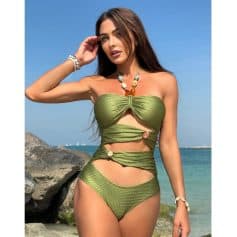 Woman in trendy green cut-out bikini at the beach, showcasing fashionable swimwear, accessories, and sunny seaside background for swimwear shopping.