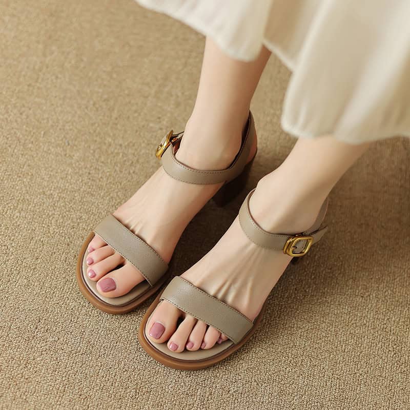 Close-up of stylish beige women’s sandals with ankle straps and gold buckles, perfect for casual and dressy occasions, displayed on a neutral carpet.