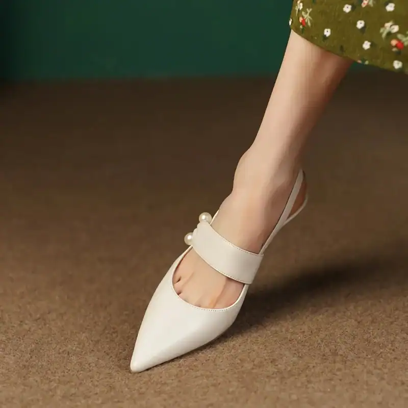 Stylish white pointed toe shoe with pearl accents and ankle strap, perfect for fashion-forward women.