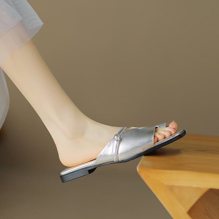Close-up of a silver flat sandal worn by a woman, showcasing trendy footwear perfect for fashion-forward individuals and comfortable, chic footwear options.