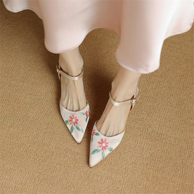 Stylish white high-heeled shoes with pink floral embroidery and ankle straps, perfect for fashionable women.