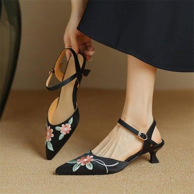 Stylish black pointed-toe heels with floral embroidery and ankle straps, perfect for fashion-forward women and special occasions.