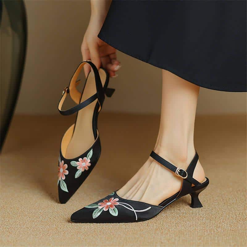 Stylish black pointed-toe heels with floral embroidery and ankle straps, perfect for fashion-forward women and special occasions.