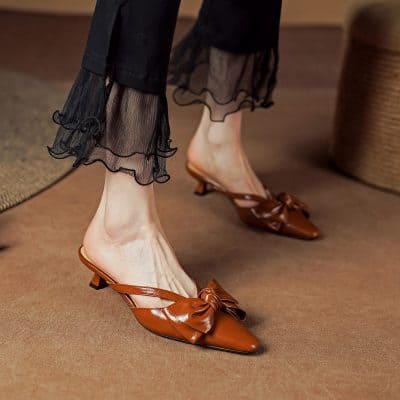 Elegant brown leather pointed-toe heels with bow detail, perfect for stylish occasions. Featuring a low heel for comfort and a trendy look. Ideal footwear for women seeking fashion and comfort.