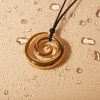 A stunning gold swirl pendant necklace with a sleek black cord displayed against a bubbly champagne-colored background, ideal for stylish jewelry lovers.