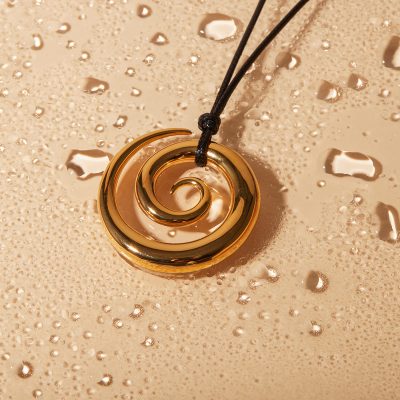 A stunning gold swirl pendant necklace with a sleek black cord displayed against a bubbly champagne-colored background, ideal for stylish jewelry lovers.