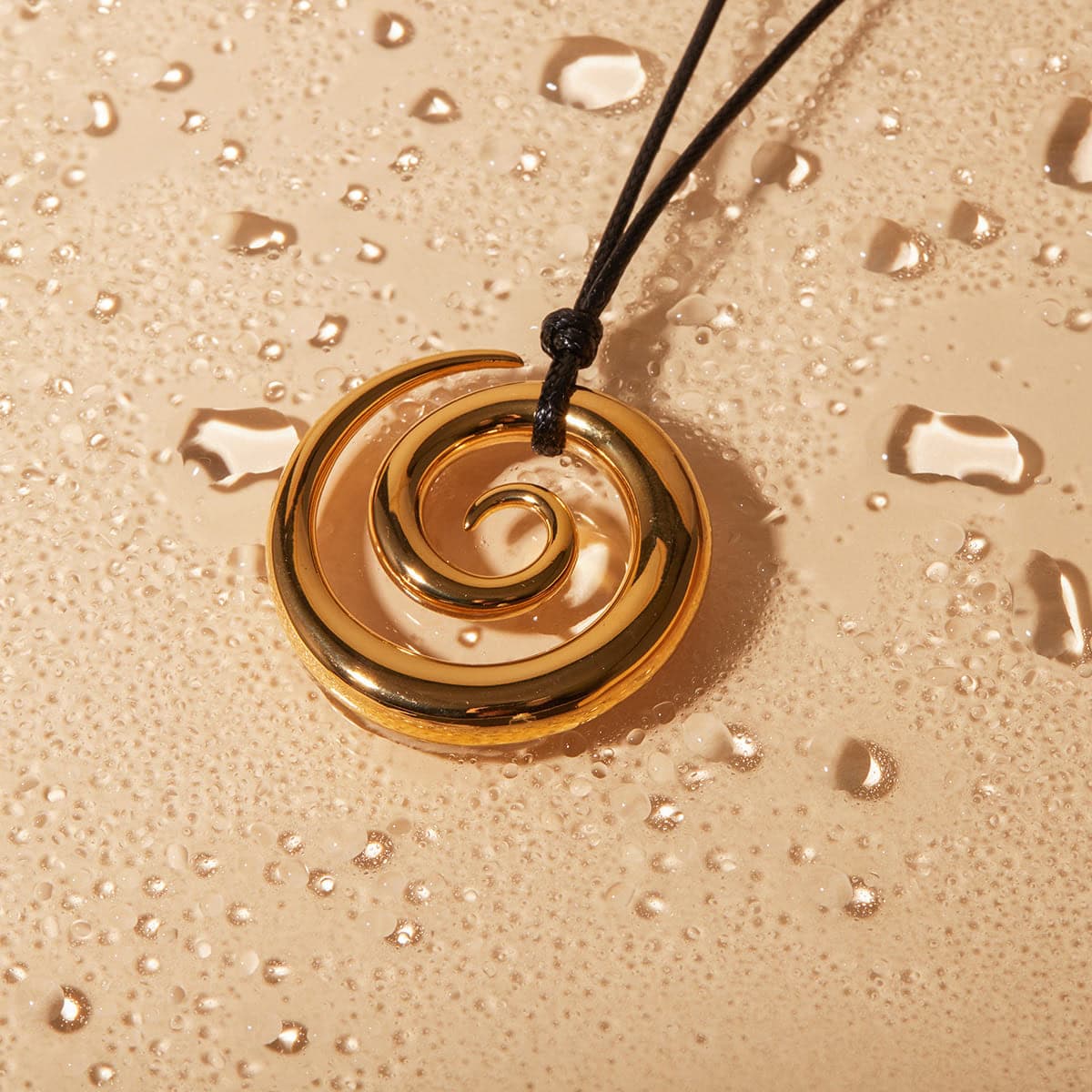 A stunning gold swirl pendant necklace with a sleek black cord displayed against a bubbly champagne-colored background, ideal for stylish jewelry lovers.